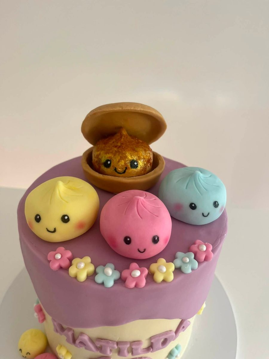 Cake topped with smiling fondant dumplings and a bao in a steamer basket, finished with pastel sugar flowers
